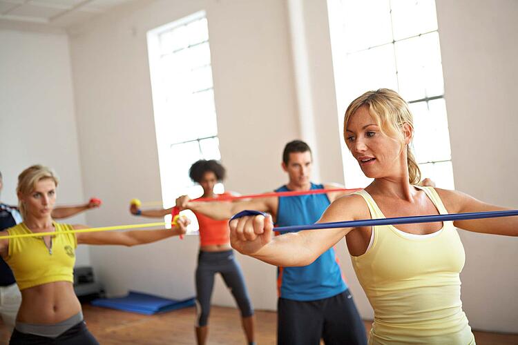 Gruppe in einem Fitnessstudio macht Übungen mit Theraband.