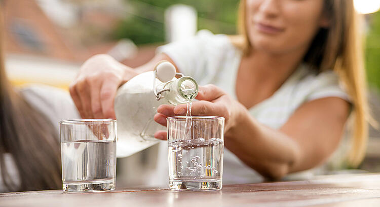 Frau schenkt sich ein Glas Wasser ein.