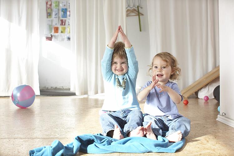Babygebärden: Zwei Kleinkinder sitzen auf dem Boden und gebärden mit ihren Händen