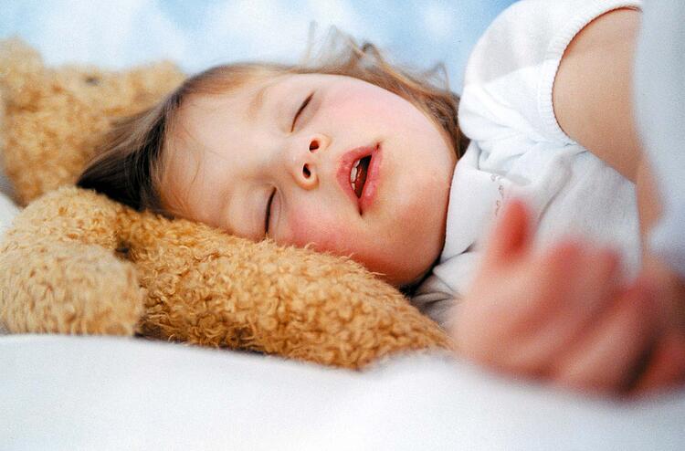 Kleines Mädchen schläft mit dem Kopf auf einem Teddybär.