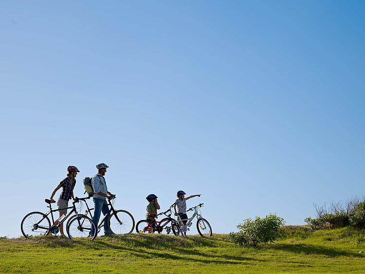 Familie macht eine Fahrradtour und steht mit Fahrrädern an einer Wiese