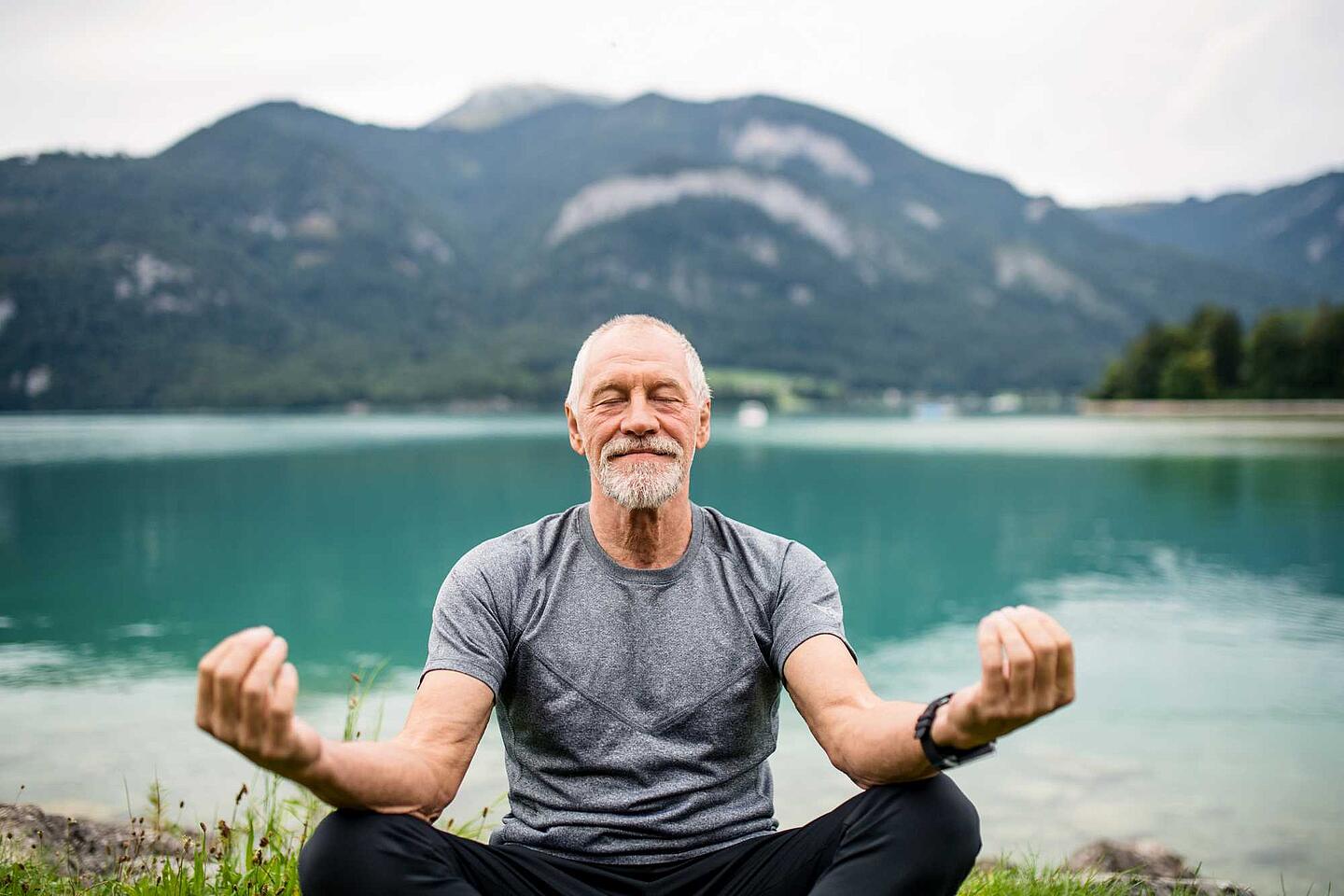 Älterer Mann macht Yoga an einem Bergsee