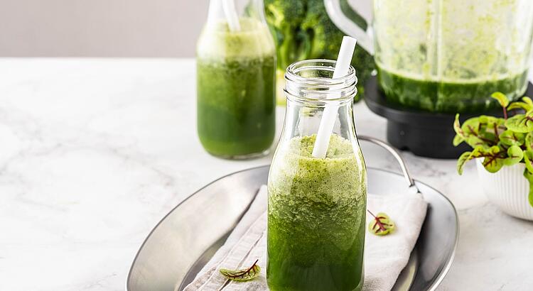 Grüner Smoothie in einer Glasflasche mit einem weißen Strohhalm.