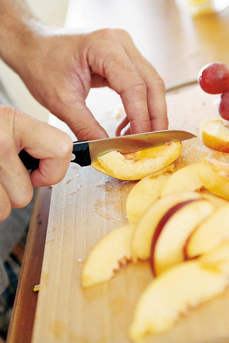 Männerhände schneiden einen Apfel in Spalten.