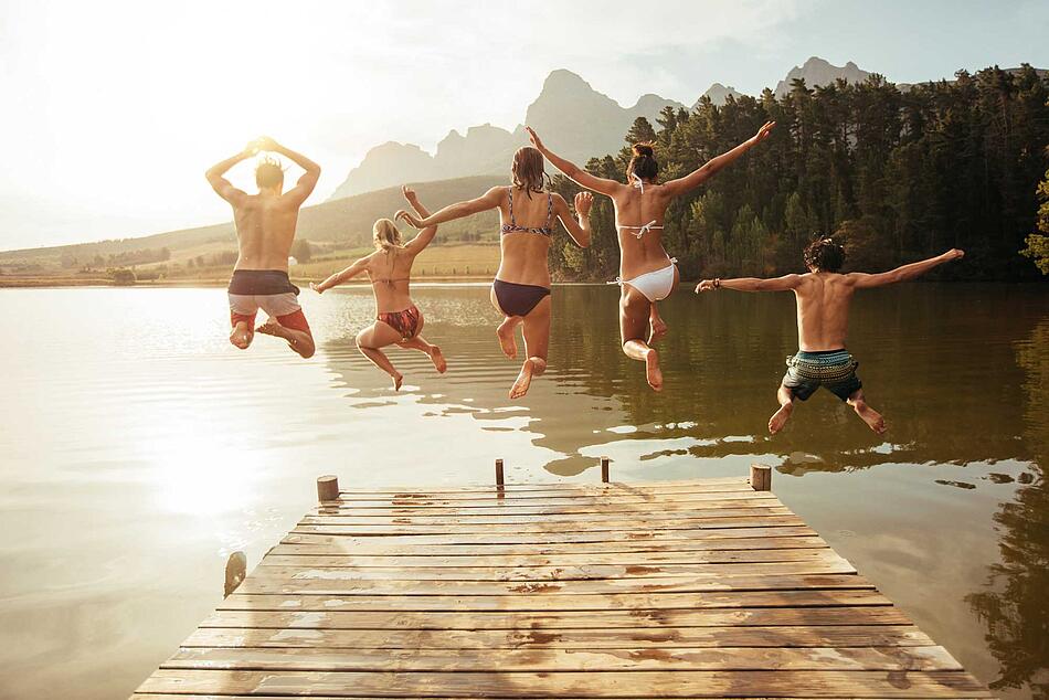 Junge Leute springen von einem Steg in einen See