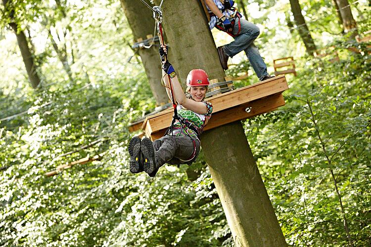 Junge Frau angeseilt im Klettergarten fährt eine Seilbahn entlang.