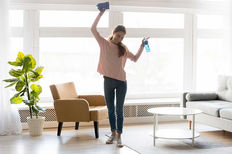 FRau mit Putzmittel und Putzlappen in der Hand tanzt durch das Wohnzimmer.