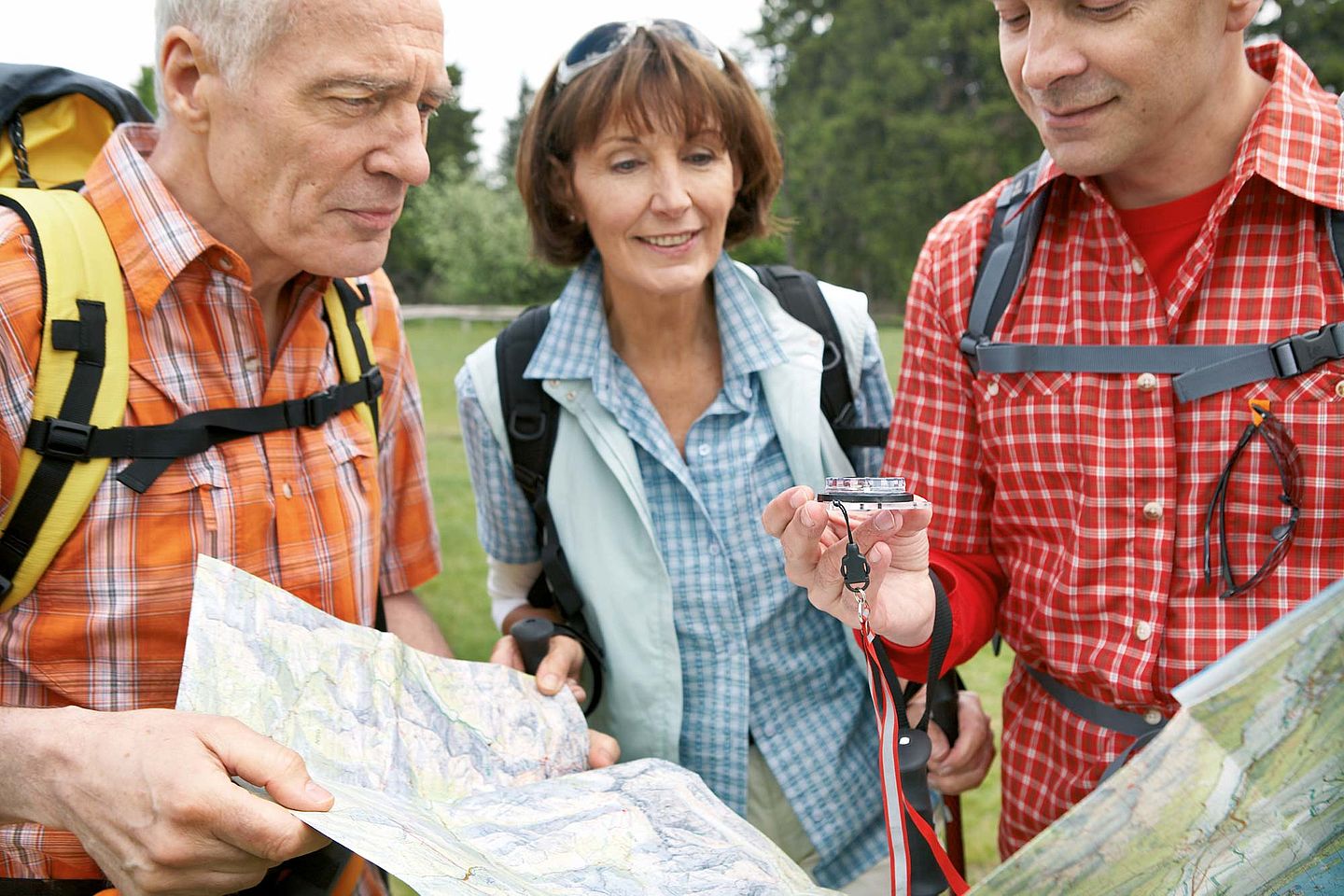 Gruppe von Wanderern mittleren Alters schauen eine Landkarte und einen Kompass an. Gruppe von Wanderern mittleren Alters schauen eine Landkarte und einen Kompass an.