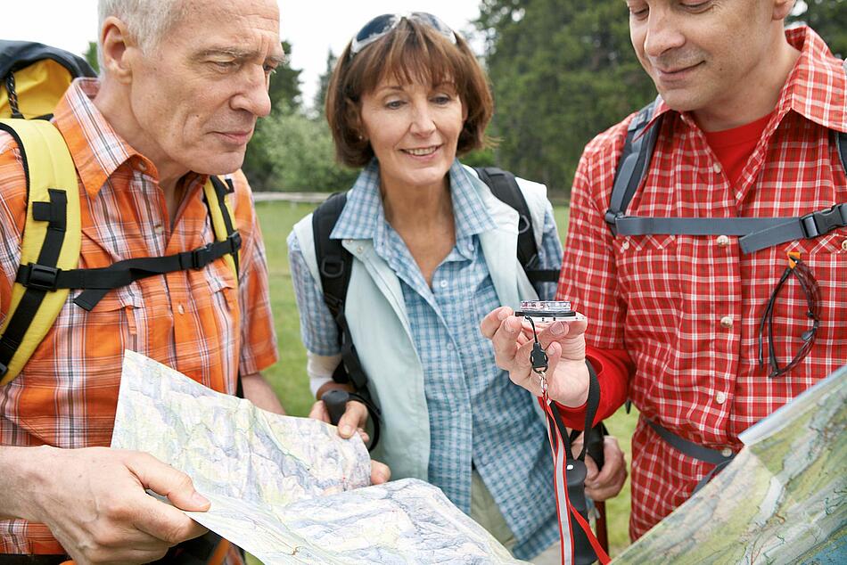 Gruppe von Wanderern mittleren Alters schauen eine Landkarte und einen Kompass an.