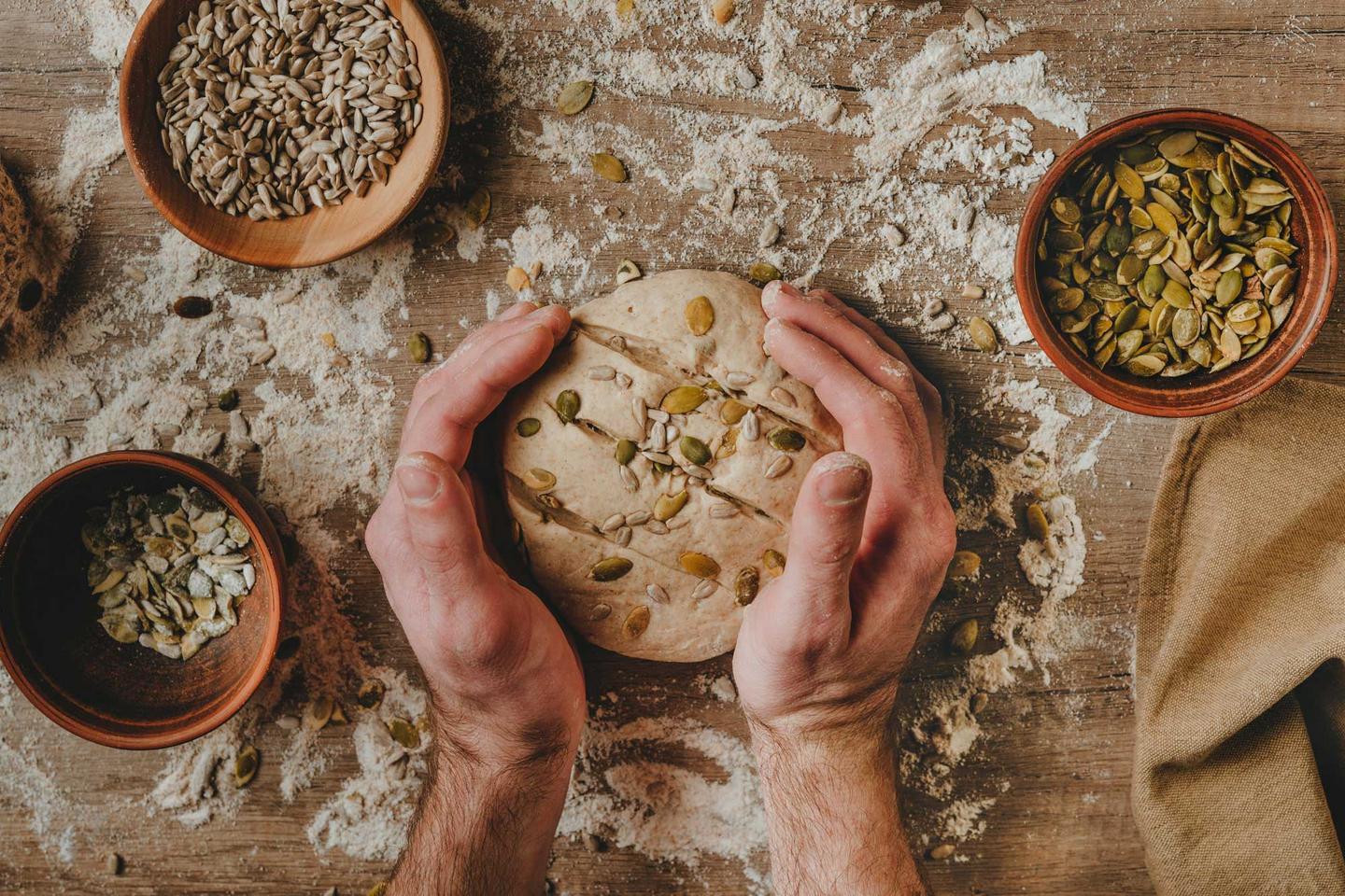 Zwei Hände formen einen Brotlaib mit Sonnnenblumenkernen