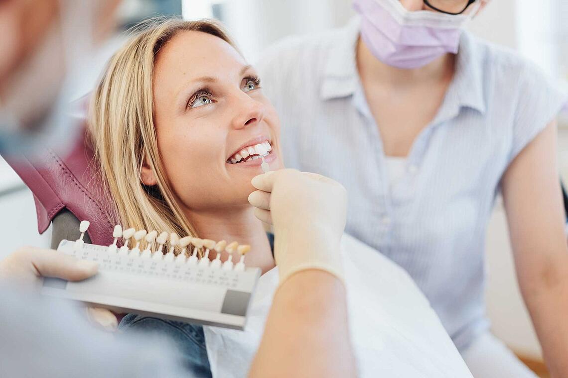 Zahnarzt prüft die Farbe der Zähne einer jungen Frau