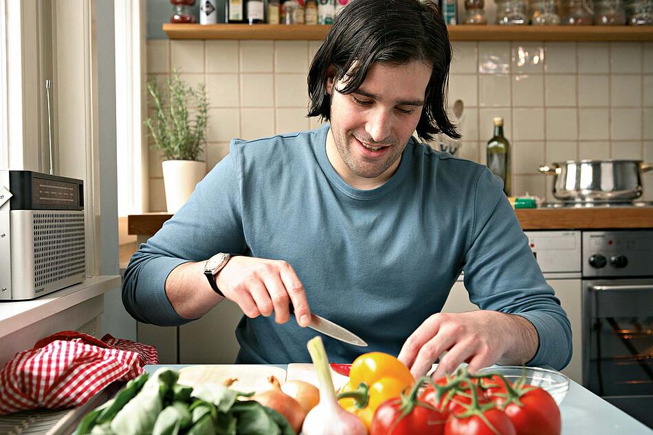 Ein Mann sitzt am Küchentisch und schneidet Gemüse.