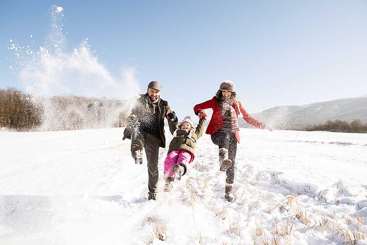 Eltern gehen mit ihrer kleinen Tochter im Schnee spazieren
