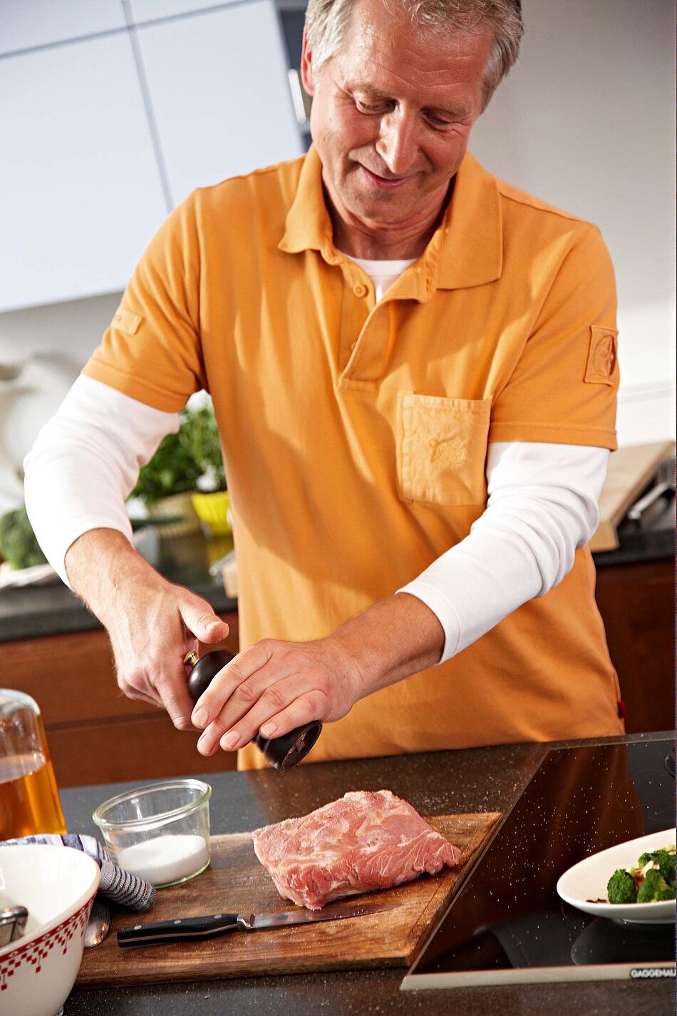 Ein Mann streut Pfeffer aus einer Mühle über ein Stück rohes Fleisch.