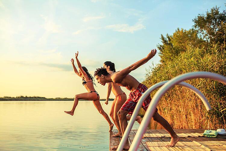 Freunde springen zusammen vom Steg in einen See