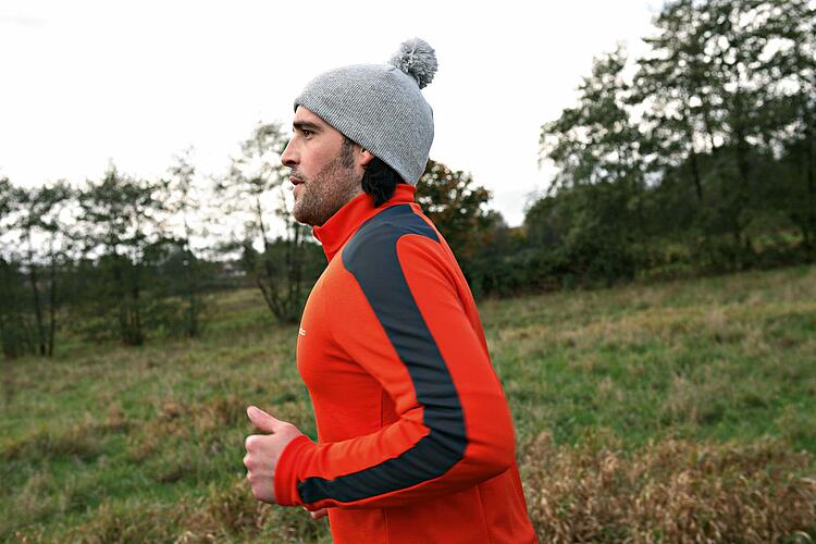 Junger Mann mit Sportkleidung und Bommelmütze beim Joggen.