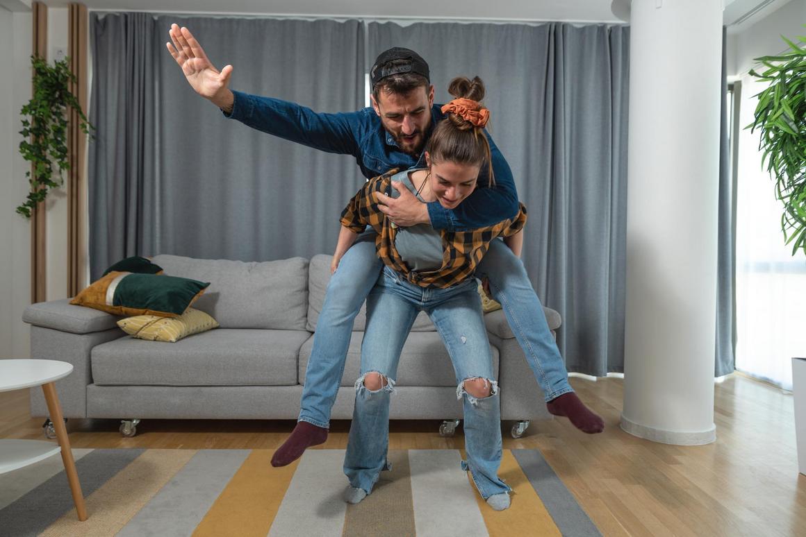 Bildnachweis: © istockphoto.com / Srdjanns74 Frau nimmt Mann im Wohnzimmer huckepack