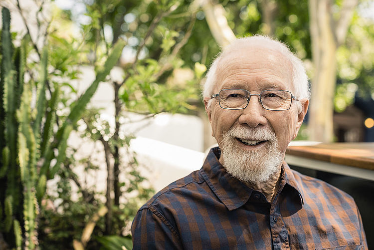 Älterer Mann mit Brille sitzt lächelnd im Garten - Bildnachweis: © wdv / Jan Lauer Älterer Mann mit Brille sitzt lächelnd im Garten