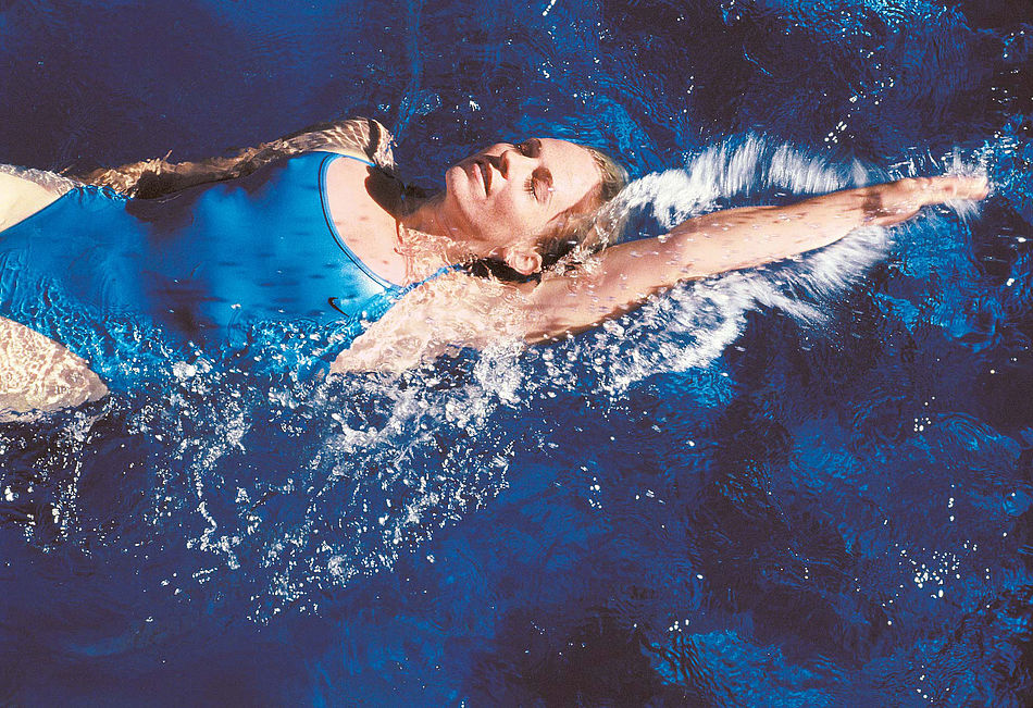 Junge Frau in einem blauen Badeanzug beim Rückenschwimmen.
