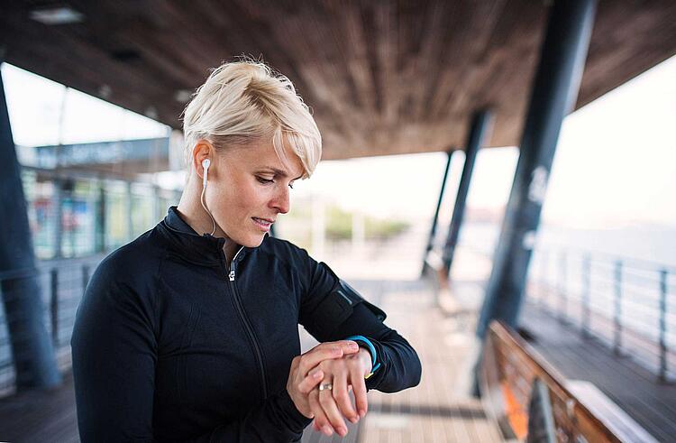 Frau schaut beim Joggen auf ihren Fitnesstracker