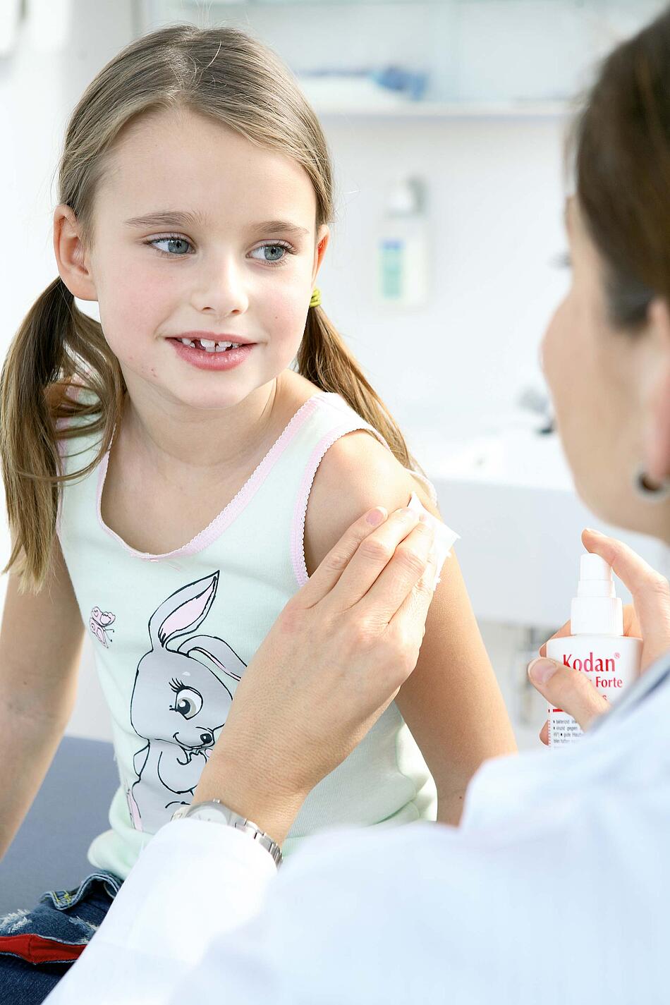 Ärztin desinfiziert den Obearm eines kleinen Mädchens.