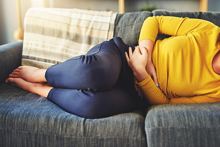 Frau liegt auf der Couch und hält die Hände auf den Bauch