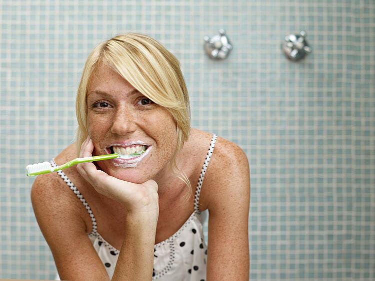 Eine Frau hat den Griff einer Zahnbürste im Mund.