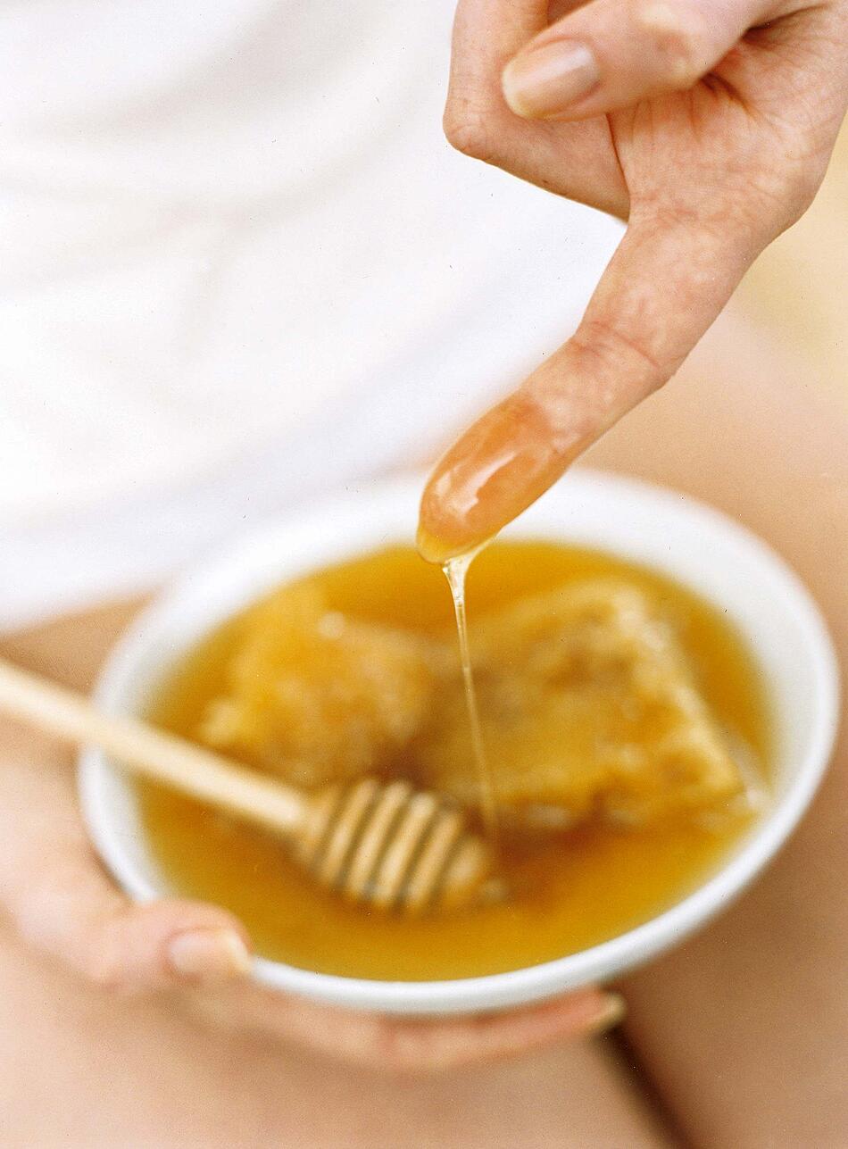 Eine Frau taucht einen Finger in eine Schüssel mit Honig.