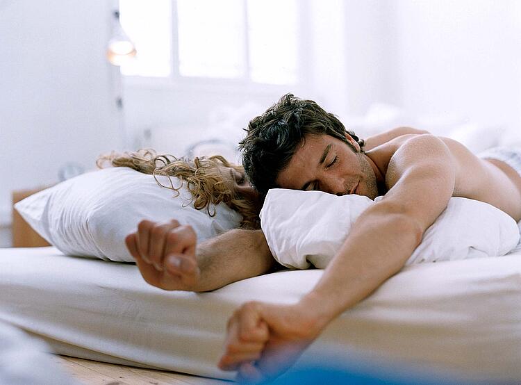 Paar liegt im Bett, der Mann wacht auf und streckt sich.