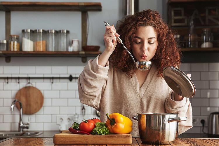 Frau kocht und probiert ihr Essen