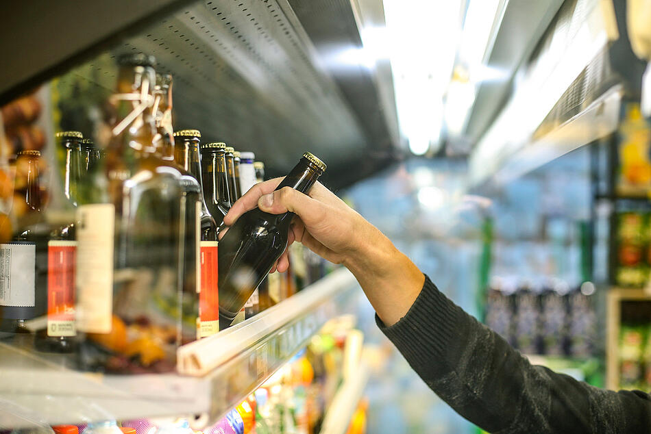 Hand nimmt eine Flasche Bier im Supermarkt aus dem Regal.