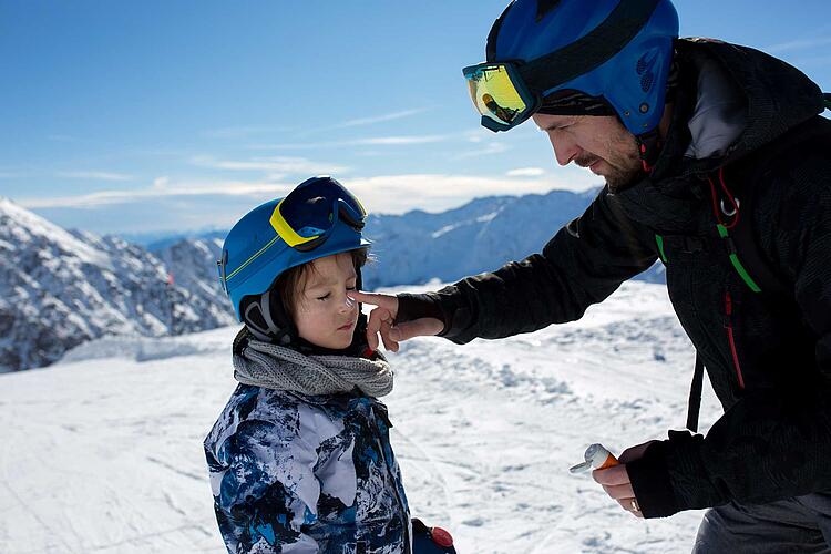 UV-Schutz beim Skifahren: Vater cremt Tochter beim Skifahren mit Sonencreme das Gesicht ein