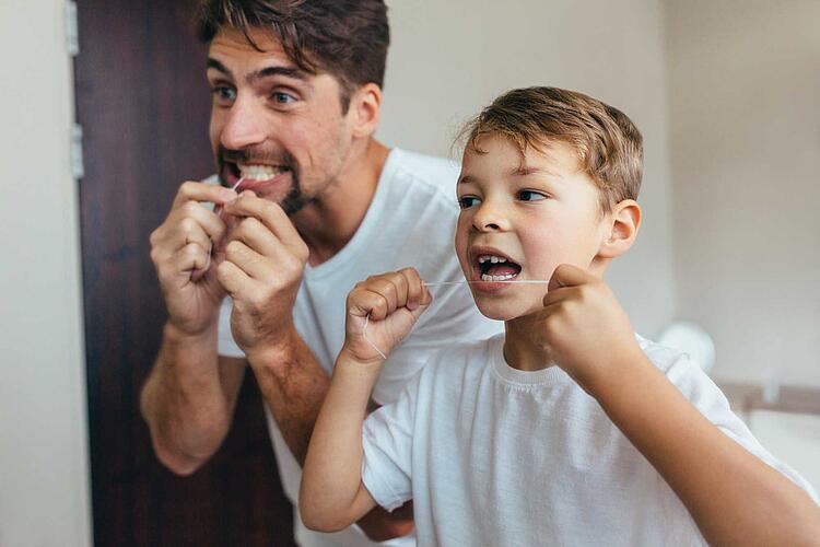 Vater und Sohn benutzen Zahnseide vor dem Spiegel