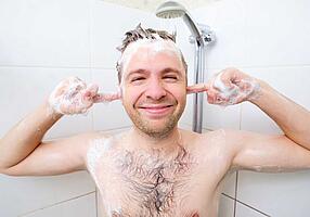 Mann eingeschäumt unter der Dusche die Finger in den Ohren