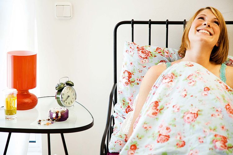 Junge Frau liegt im Bett und lacht. / Oana Szekely Junge Frau liegt im Bett und lacht.
