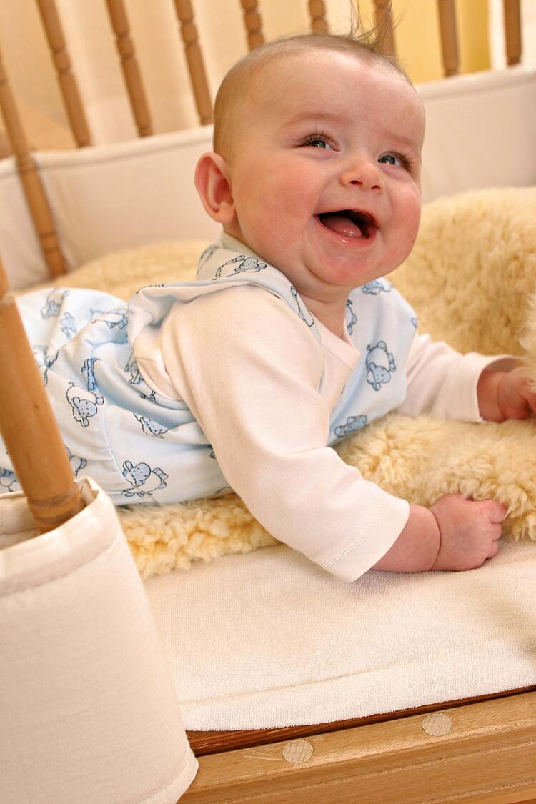 Lachendes Baby liegt auf dem Bauch in einem Gitterbett und hebt den Kopf.