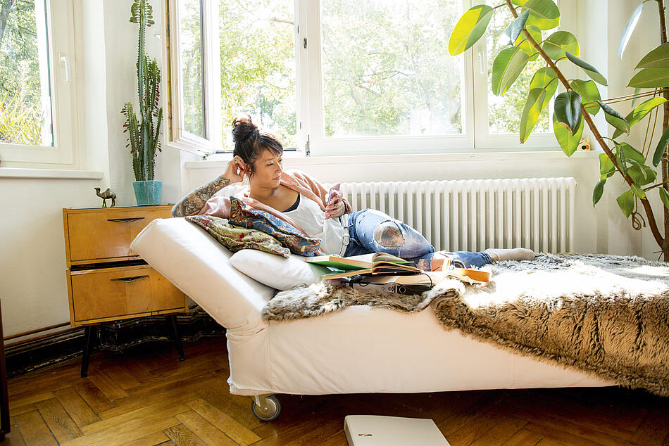 Junge Frau liegt auf der Couch und schaut beim lernen auf ihr Handy.