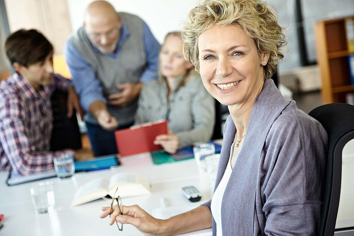 Frau an einem Konferenztisch lächelt in die Kamera.