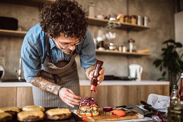 Mann macht Ketchup auf einen Burger