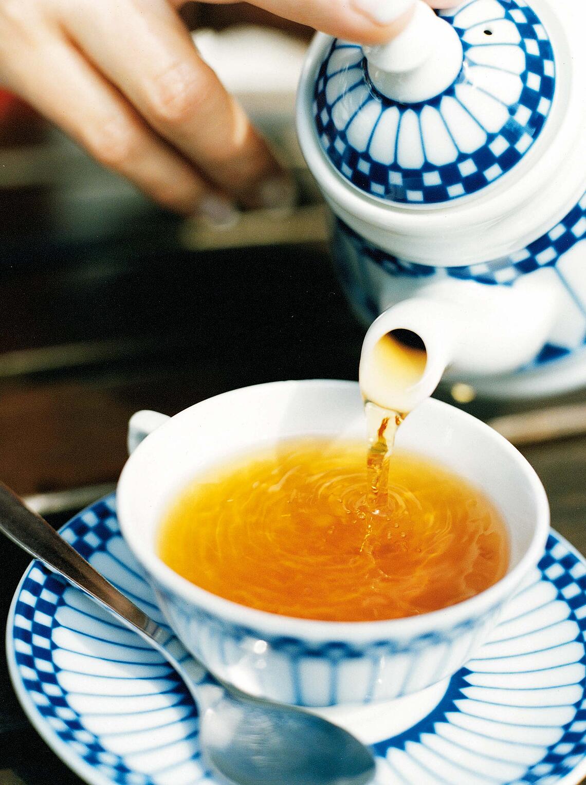 Frauenhand gießt aus einer Teekanne Tee in eine Tasse.