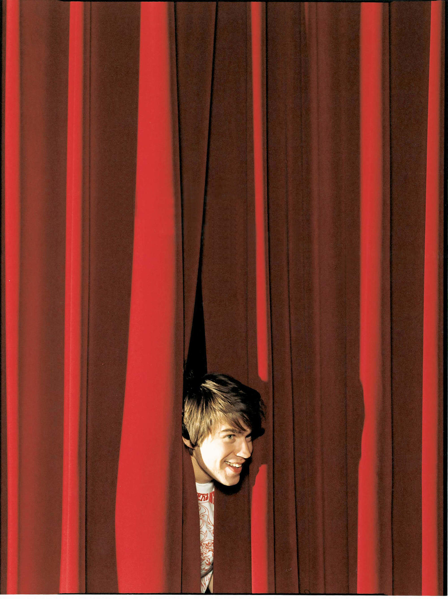 Jugendlicher schaut durch einen roten Theatervorhang. Jugendlicher schaut durch einen roten Theatervorhang.