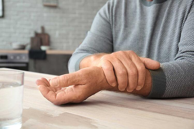 Mann mit Parkinson legt seine Hand über seinen Unterarm