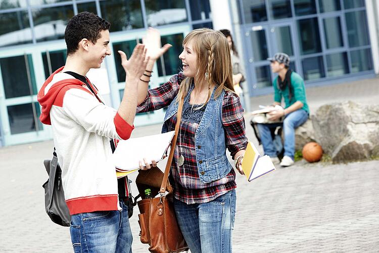 Junge und Mädchen begrüßen sich auf dem Schulhof mit abklatschen.