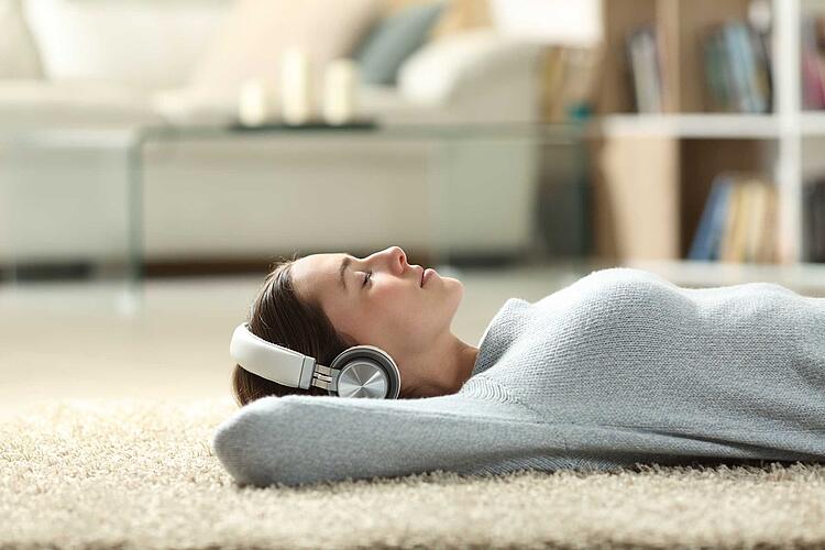 Frau  mit Kopfhörern liegt entspannt auf dem Teppich 