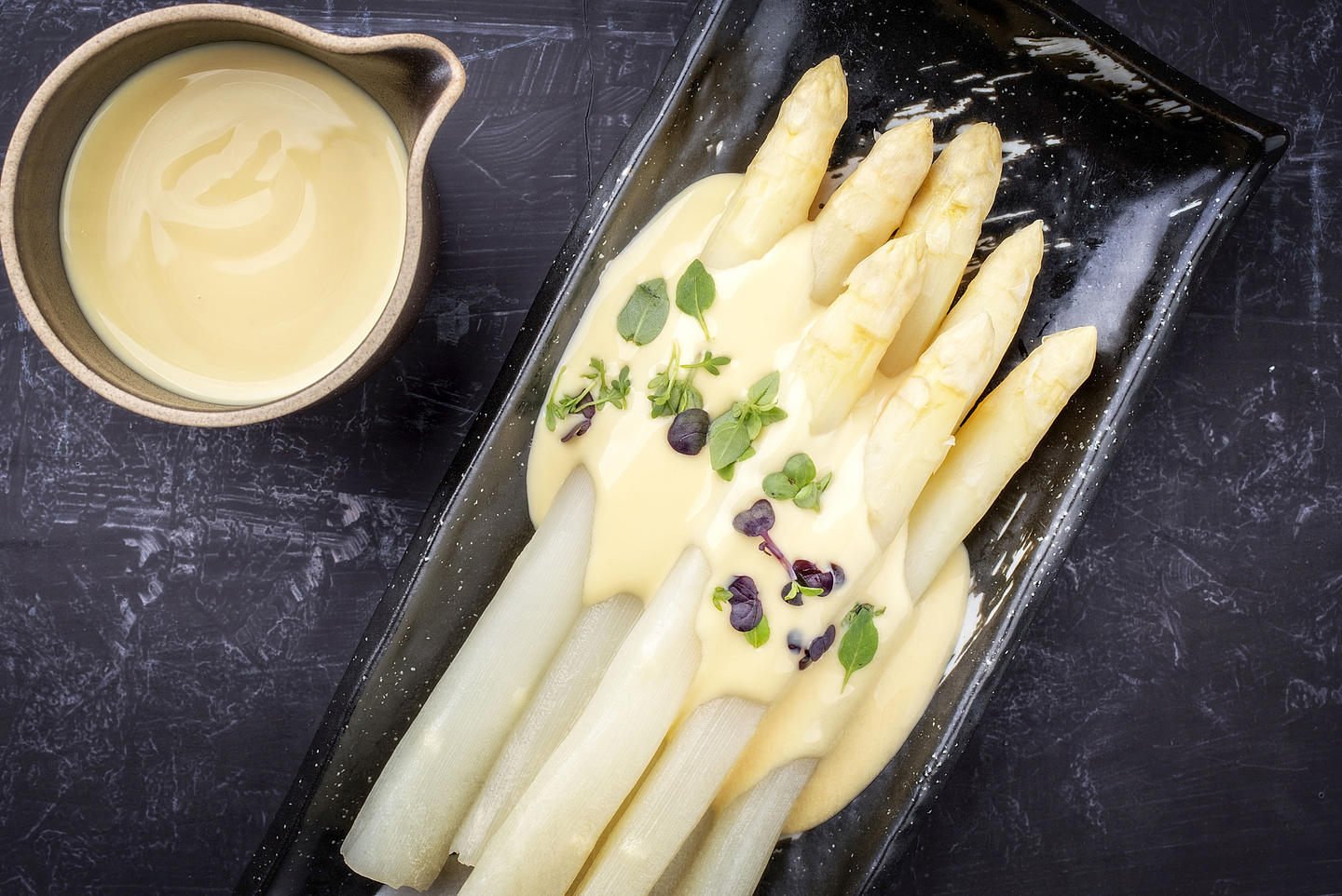 Gekochter Spargel mit Sauce Hollandaise auf einem schwarzen Teller.