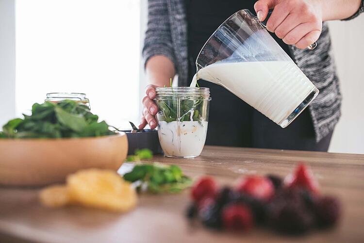 Eine Hand gießt Milch aus einem Krug in ein Glas mit Kräutern.