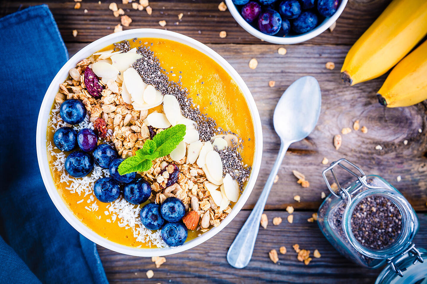 Müsli mit frischen Früchten und Nüssen in einer Schüssel, daneben ein Löffel und ein Glas Chiasamen.