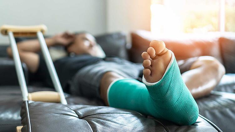 Mann mit bandagiertem Bein liegt auf dem Bett.