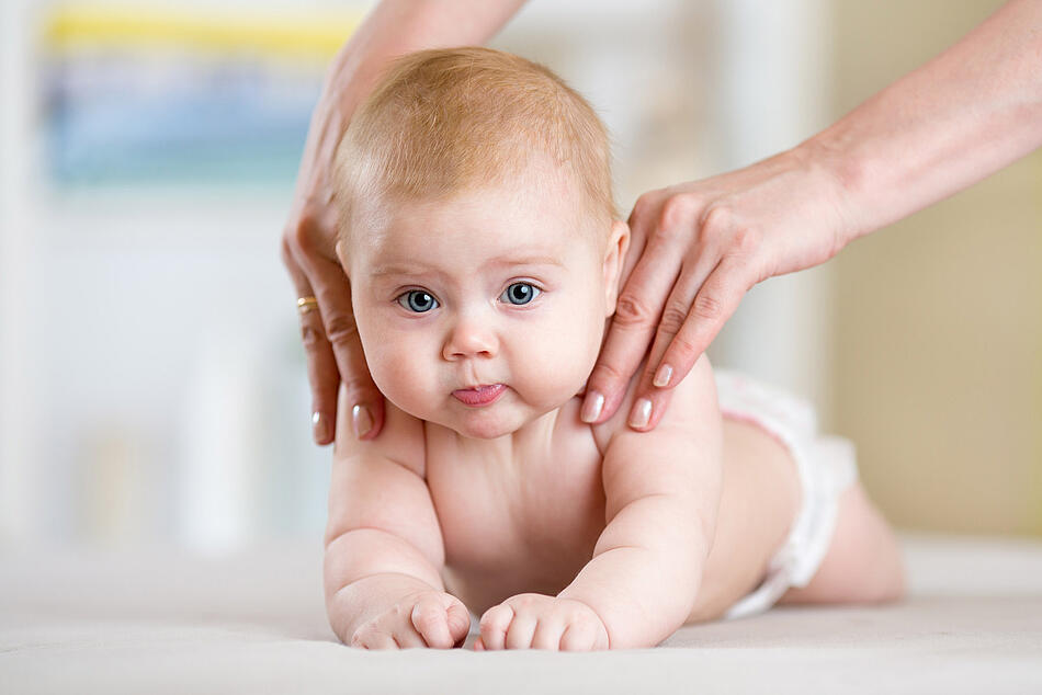 Ein Baby liegt auf dem Bauch und wird sanft massiert.