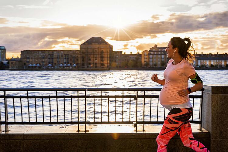 Schwangere joggt in der Stadt an einem Flußufer bei Sonnenuntergang.